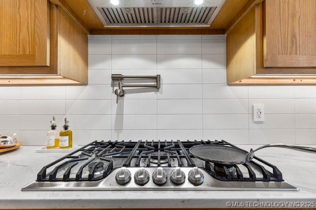 interior details featuring stainless steel gas stovetop, exhaust hood, backsplash, and light stone counters