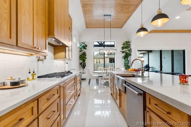 kitchen with sink, stainless steel appliances, light stone countertops, decorative backsplash, and decorative light fixtures