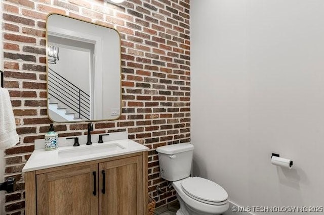 bathroom featuring brick wall, toilet, and vanity