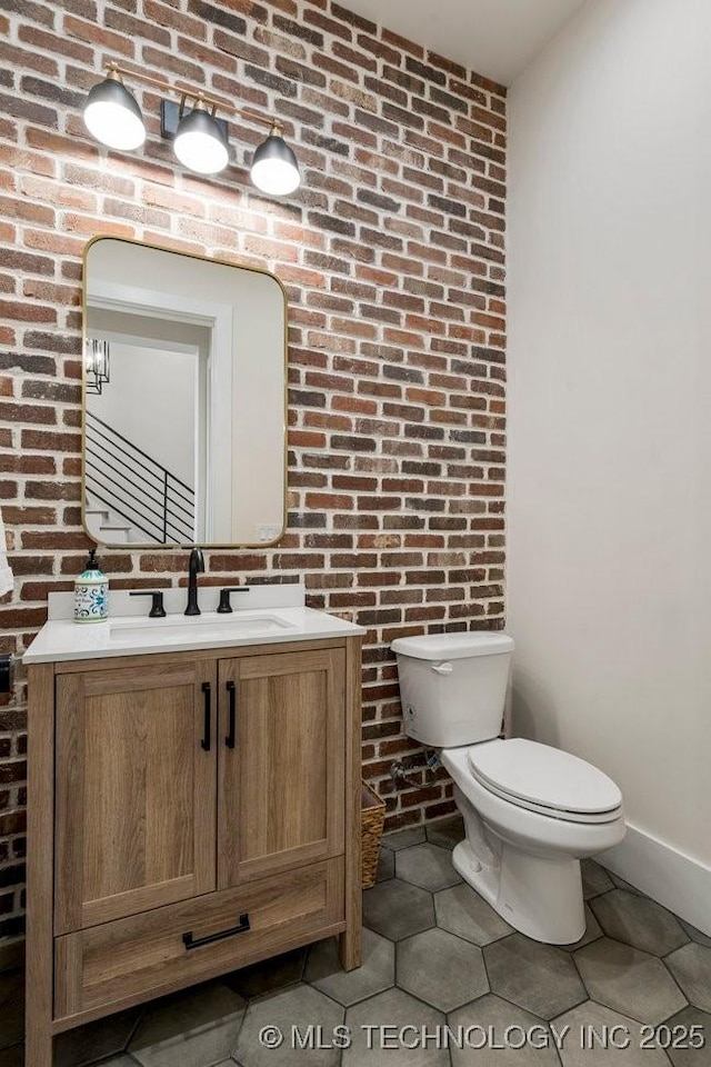 bathroom with vanity, toilet, and brick wall