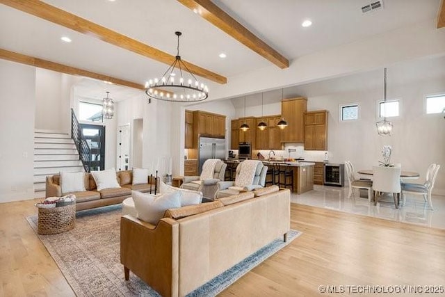 living room with a towering ceiling, a notable chandelier, beverage cooler, beamed ceiling, and light wood-type flooring