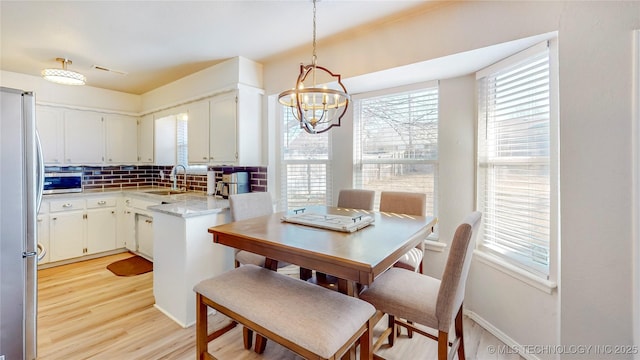 kitchen featuring decorative light fixtures, tasteful backsplash, white cabinetry, stainless steel appliances, and light wood-type flooring