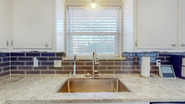 interior details featuring white cabinetry, sink, backsplash, and light stone countertops