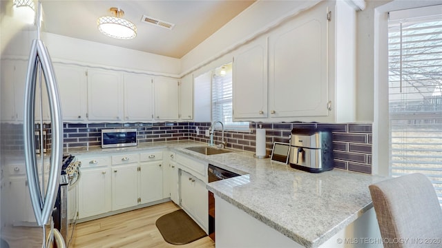 kitchen featuring sink, white cabinetry, kitchen peninsula, stainless steel appliances, and decorative backsplash