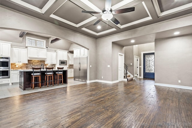 unfurnished living room with beamed ceiling, coffered ceiling, hardwood / wood-style floors, and ceiling fan