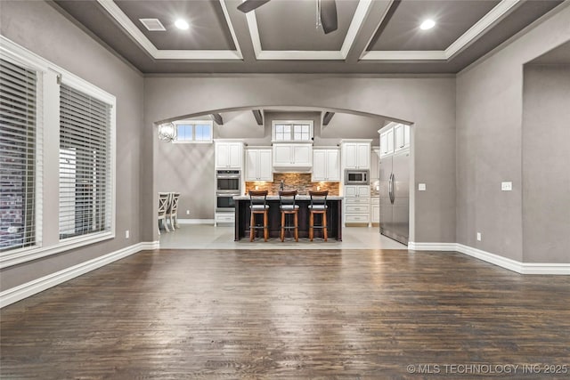 unfurnished living room with coffered ceiling, ceiling fan, dark hardwood / wood-style flooring, and beam ceiling