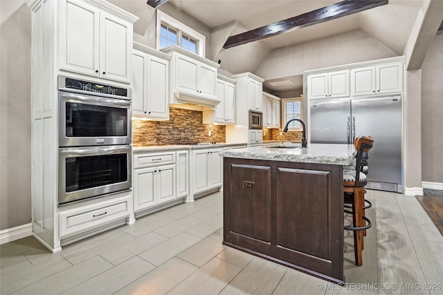 kitchen with built in appliances, sink, a kitchen island with sink, and white cabinets