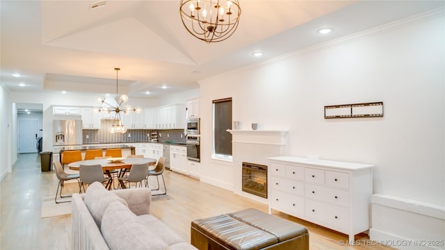 living room featuring an inviting chandelier, a tray ceiling, light hardwood / wood-style flooring, and ornamental molding