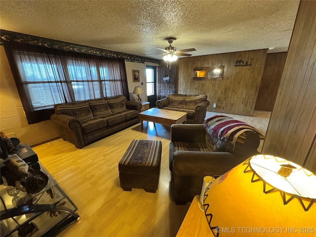 living room featuring hardwood / wood-style flooring, ceiling fan, wooden walls, and a textured ceiling