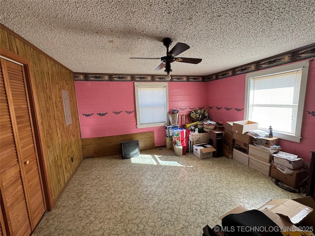 interior space featuring ceiling fan, a textured ceiling, and wood walls