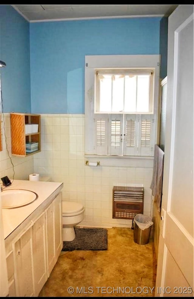 bathroom with tile walls, heating unit, vanity, an enclosed shower, and toilet