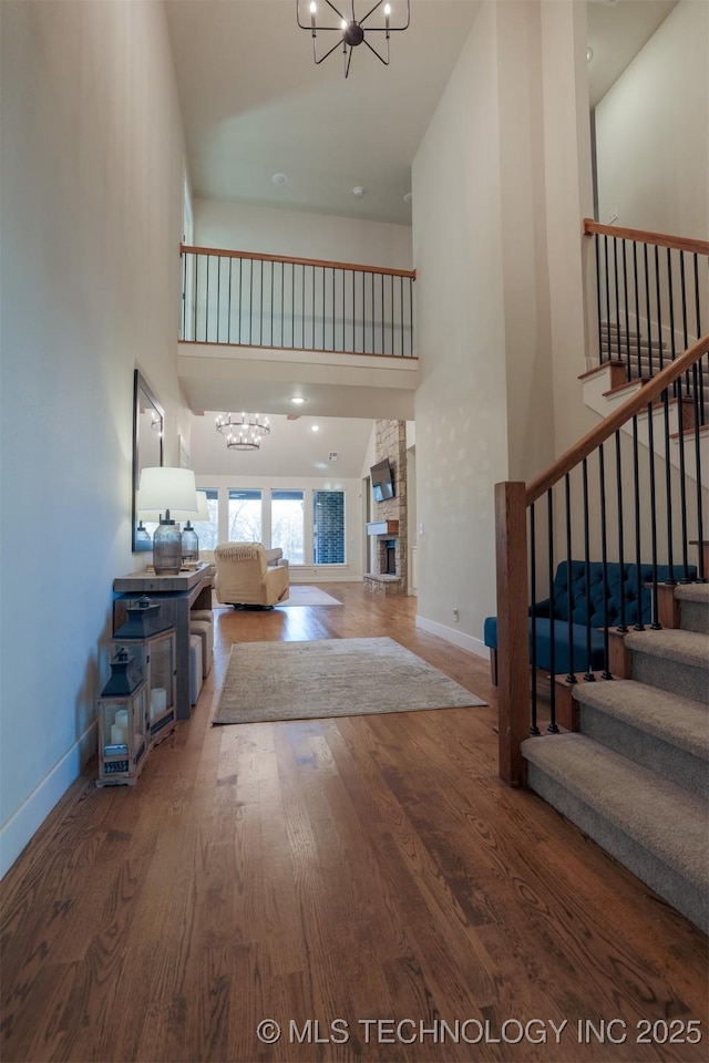 entryway featuring hardwood / wood-style flooring, a towering ceiling, a notable chandelier, and a fireplace