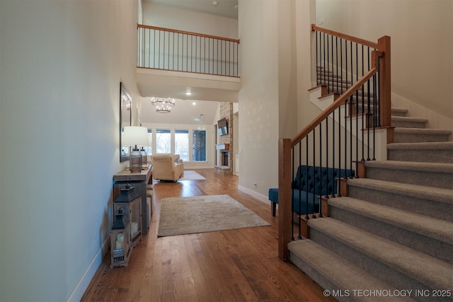 foyer featuring an inviting chandelier, a fireplace, a towering ceiling, and wood-type flooring