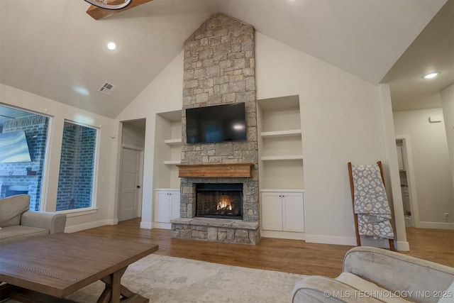 living room featuring built in features, a fireplace, and light hardwood / wood-style flooring