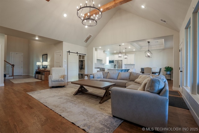 living room with high vaulted ceiling, a barn door, hardwood / wood-style floors, and an inviting chandelier