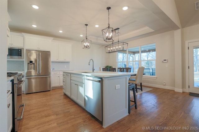 kitchen with appliances with stainless steel finishes, decorative light fixtures, white cabinetry, sink, and a center island with sink