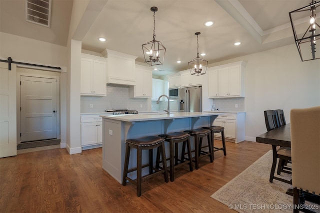 kitchen featuring pendant lighting, appliances with stainless steel finishes, an island with sink, white cabinets, and a barn door