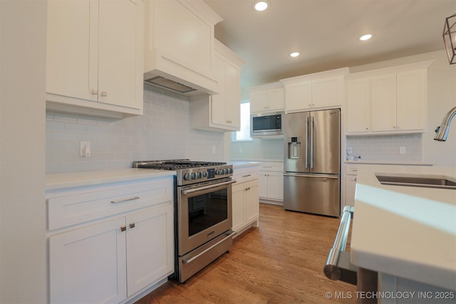 kitchen with premium range hood, white cabinetry, sink, stainless steel appliances, and light hardwood / wood-style flooring