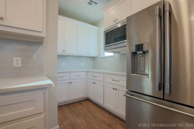 kitchen with built in microwave, white cabinets, decorative backsplash, stainless steel refrigerator with ice dispenser, and dark wood-type flooring