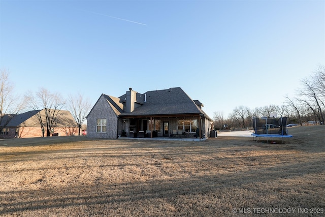 rear view of property with central AC unit, a trampoline, and a lawn