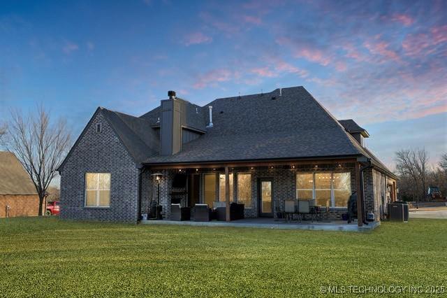 back house at dusk featuring a lawn and a patio area