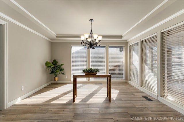 interior space with crown molding, hardwood / wood-style flooring, a raised ceiling, and a chandelier