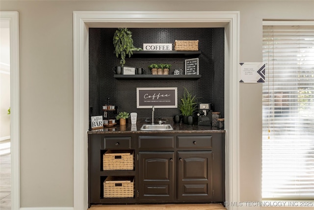 bar featuring sink, dark stone countertops, and dark brown cabinetry