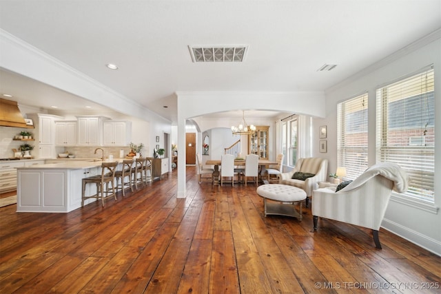 living room featuring dark hardwood / wood-style flooring, crown molding, sink, and a chandelier