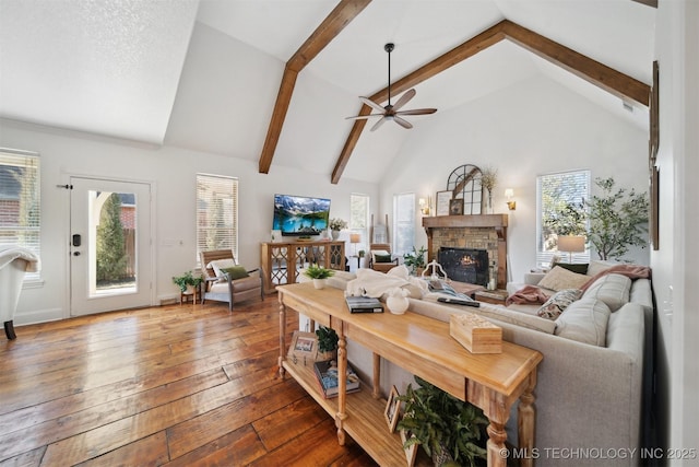 living room with a stone fireplace, high vaulted ceiling, beamed ceiling, hardwood / wood-style flooring, and ceiling fan