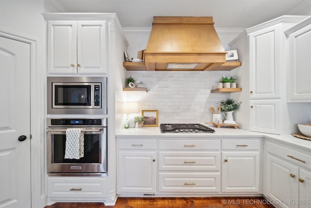 kitchen with tasteful backsplash, premium range hood, white cabinets, and appliances with stainless steel finishes