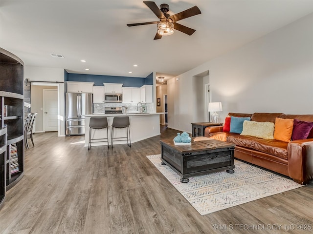 living room featuring ceiling fan, sink, a barn door, and light hardwood / wood-style floors