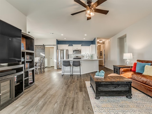 living room featuring sink, a barn door, ceiling fan, and light wood-type flooring