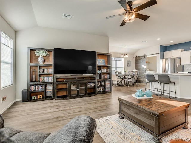 living room with a barn door, ceiling fan, lofted ceiling, and light wood-type flooring