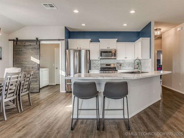 kitchen featuring appliances with stainless steel finishes, tasteful backsplash, sink, white cabinets, and a barn door