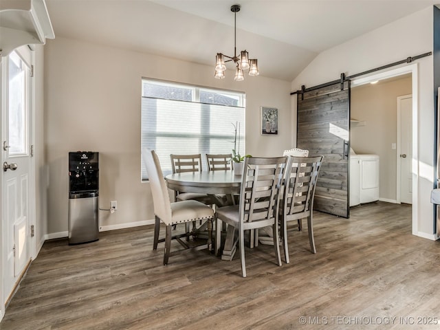 dining space with lofted ceiling, wood-type flooring, a chandelier, washer / clothes dryer, and a barn door