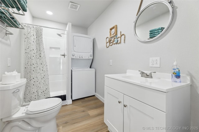 bathroom featuring hardwood / wood-style floors, stacked washer / dryer, vanity, curtained shower, and toilet