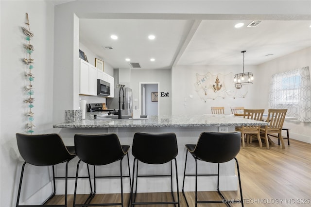 kitchen with decorative light fixtures, white cabinets, kitchen peninsula, stainless steel appliances, and light hardwood / wood-style flooring