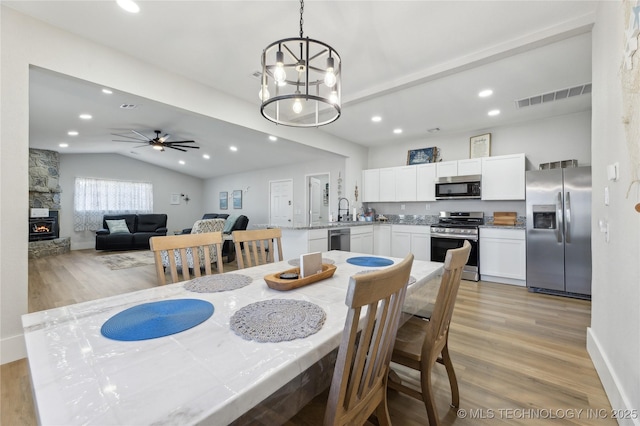 dining space featuring lofted ceiling, a stone fireplace, sink, light hardwood / wood-style flooring, and ceiling fan with notable chandelier