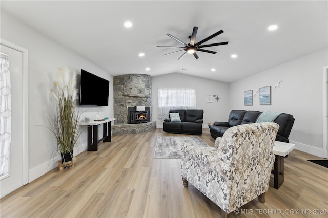 living room featuring ceiling fan, lofted ceiling, a stone fireplace, and light hardwood / wood-style flooring