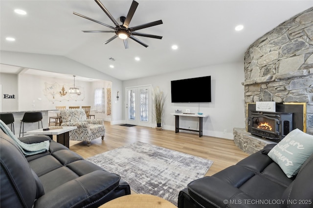 living room featuring vaulted ceiling, a fireplace, ceiling fan with notable chandelier, and light hardwood / wood-style floors