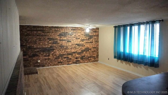 unfurnished room featuring ceiling fan, hardwood / wood-style flooring, a textured ceiling, and brick wall