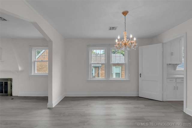 unfurnished dining area featuring heating unit, an inviting chandelier, and light hardwood / wood-style flooring