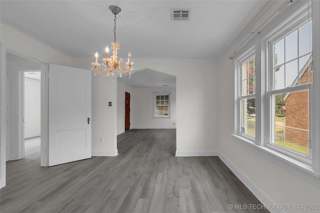 unfurnished dining area featuring wood-type flooring, plenty of natural light, and a chandelier