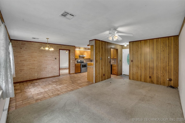 unfurnished living room with brick wall, ceiling fan with notable chandelier, light carpet, and wood walls