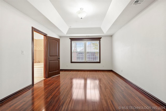 unfurnished bedroom featuring connected bathroom, a tray ceiling, and dark hardwood / wood-style floors