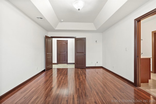 unfurnished bedroom with wood-type flooring and a raised ceiling