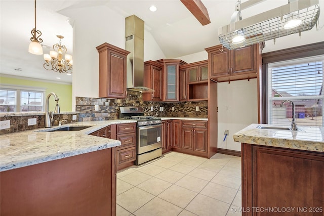 kitchen featuring gas range, decorative light fixtures, sink, and wall chimney range hood