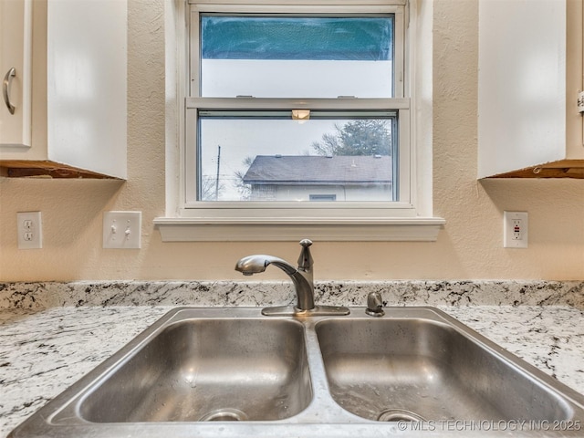 room details featuring white cabinetry, light stone countertops, and sink