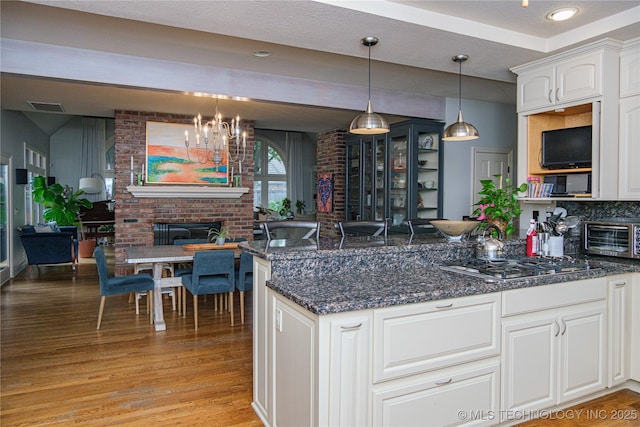 kitchen with pendant lighting, white cabinetry, a fireplace, stainless steel gas cooktop, and light wood-type flooring