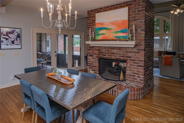 dining area with hardwood / wood-style flooring, an inviting chandelier, a fireplace, and french doors